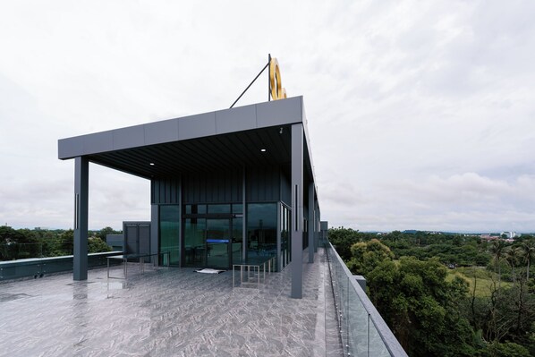 A modern building with a glass facade and a covered terrace. - One Budget Hotel Chiangrai Baanmai (Chiang Rai)