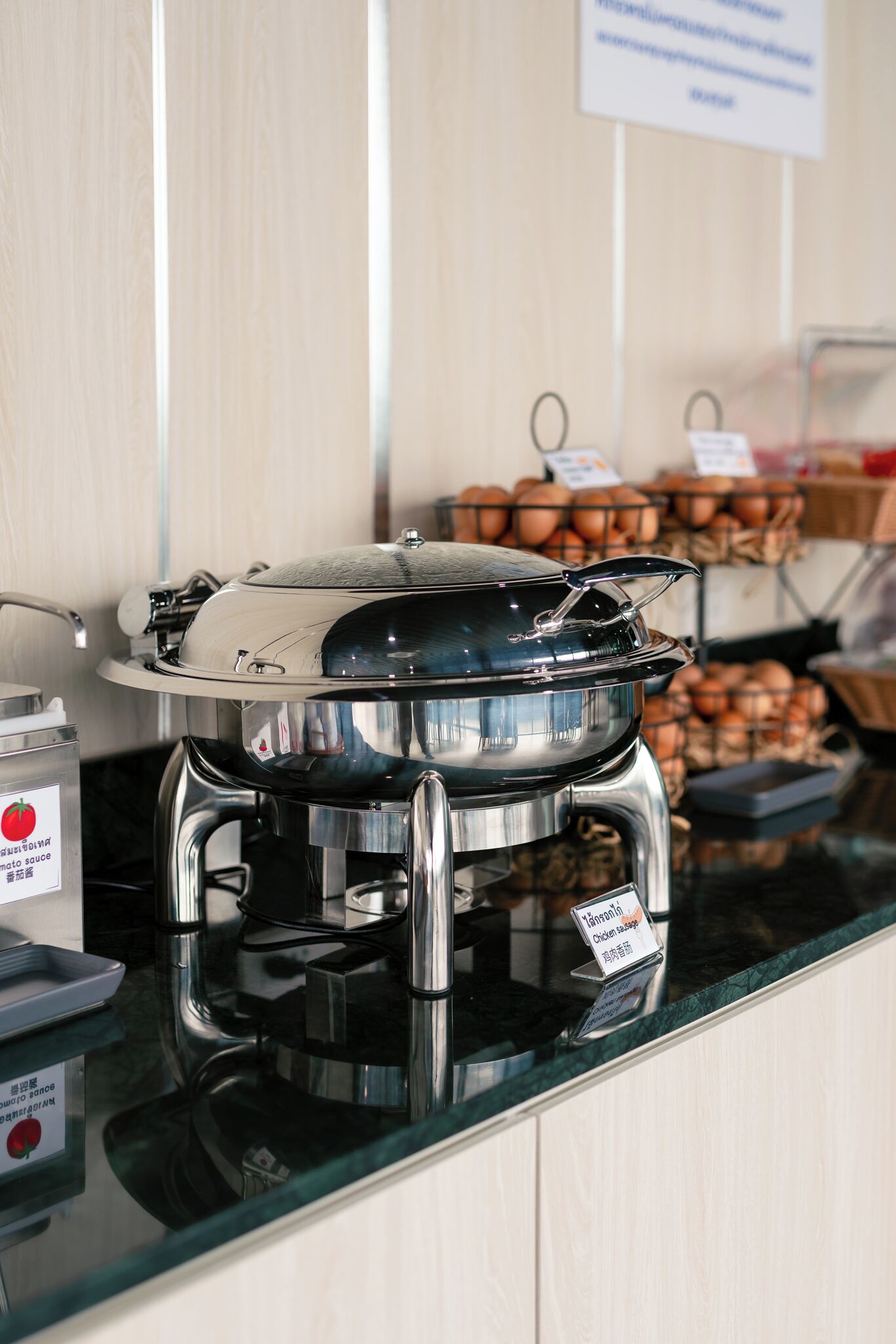Un buffet avec un présentoir à aliments couvert, un panneau indiquant la possibilité d’opter pour une sauce tomate, et, au fond, une présentation d’œufs.