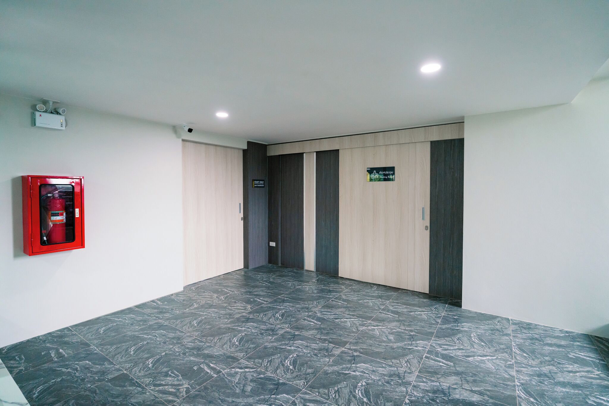 A spacious hallway with dark marble flooring, a red fire extinguisher, and a sign indicating the direction to the elevator.