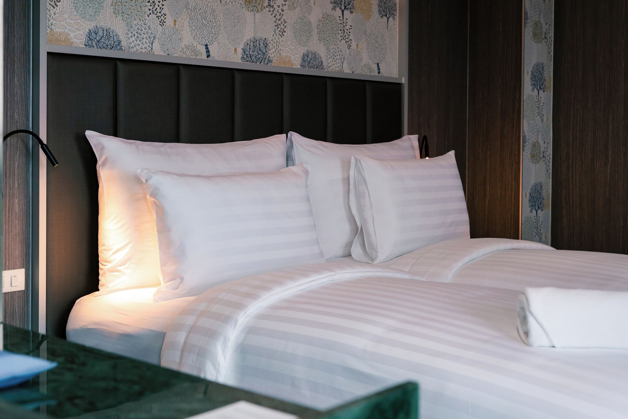 Una cama bien hecha con sábanas blancas y un cabecero con estampado floral.