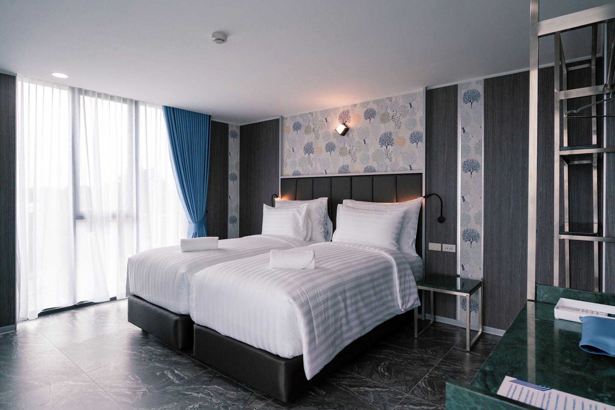 Habitación de hotel moderna con una cama grande, una mesita de noche, un escritorio y vistas de la ciudad a través de amplias ventanas.
