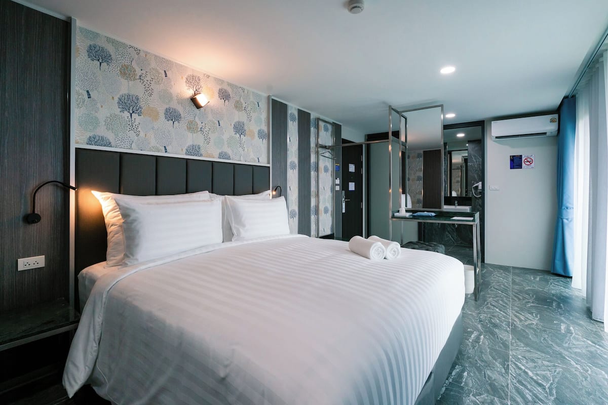 A hotel room with a large bed, a bedside table, a mirror, a bathroom with a sink, and a shower.