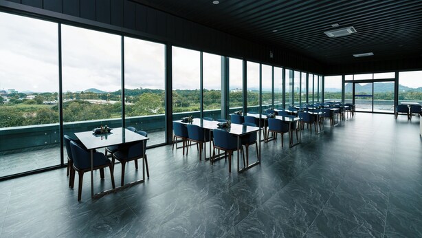 A modern dining area with large windows, multiple tables, and chairs. - One Budget Hotel Chiangrai Baanmai (Chiang Rai)