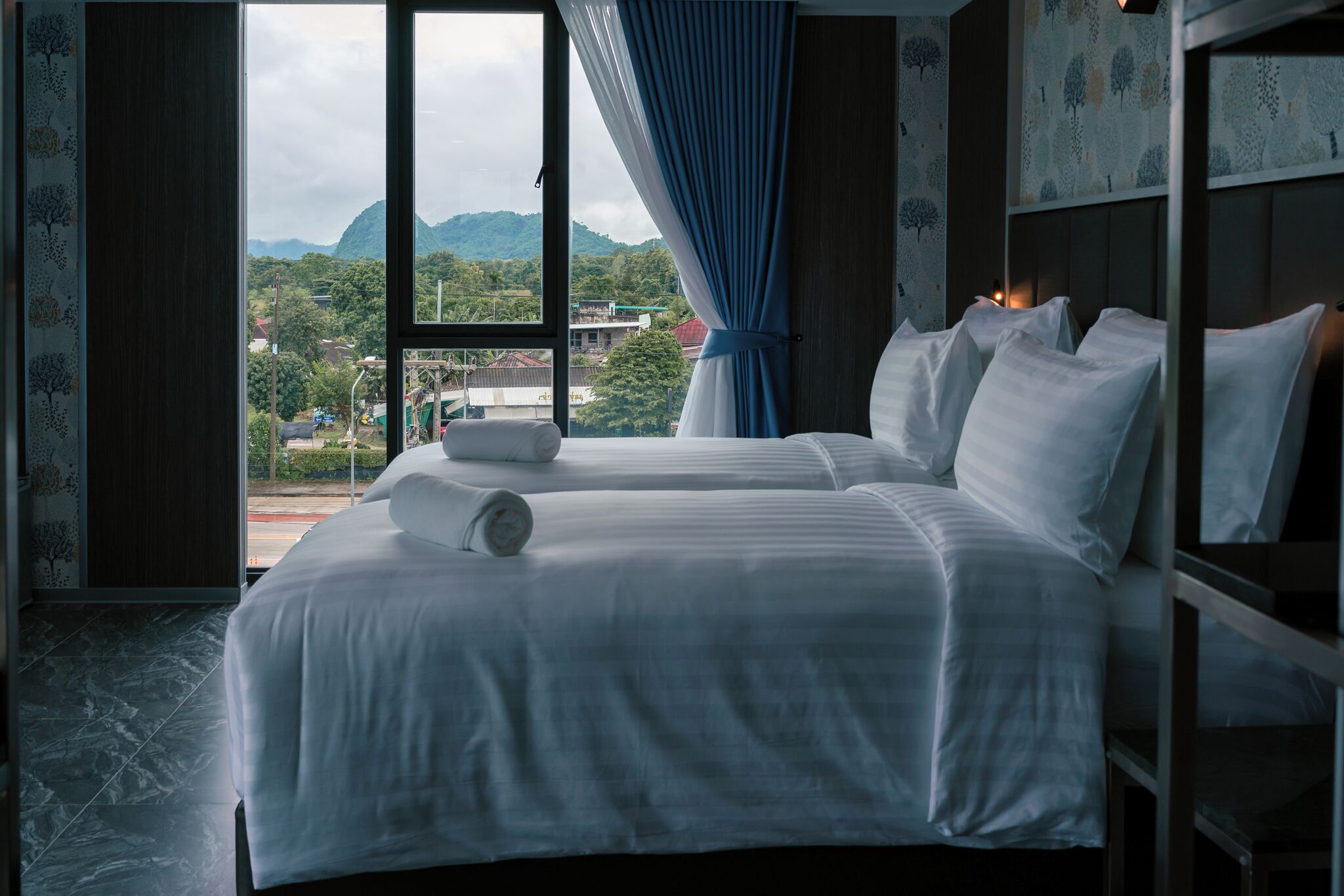 A hotel room with a large bed, a view of the mountains, and a window with curtains.