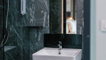 Een moderne badkamer met een marmeren wand, een witte wasbak en een handdouche.
