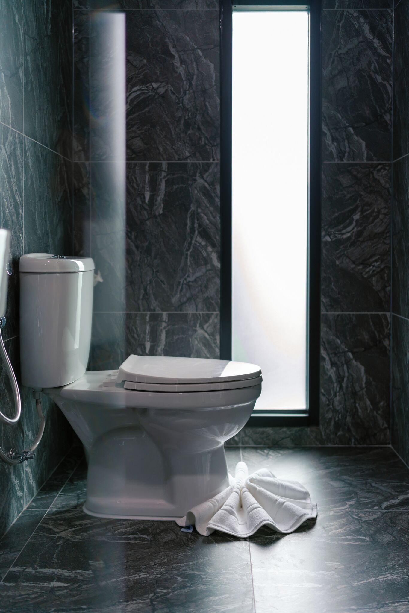 A modern bathroom with a marble floor, a white toilet, and a window providing natural light.