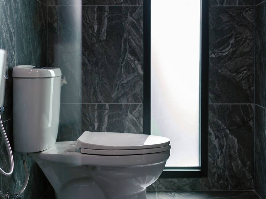 A modern bathroom with a marble floor, a white toilet, and a window providing natural light.