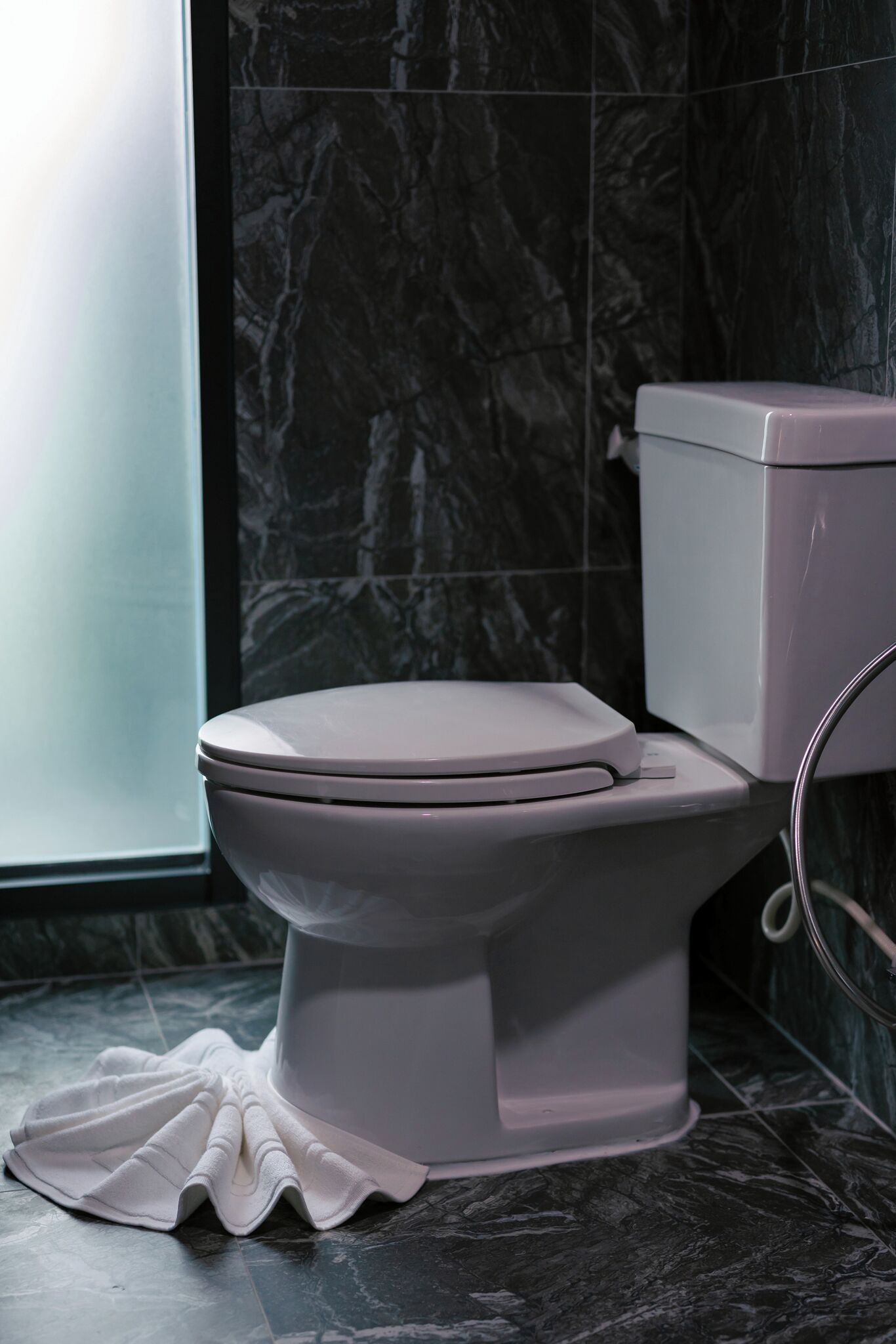 A modern toilet with a white lid and tank, positioned next to a marble wall and a glass shower enclosure.