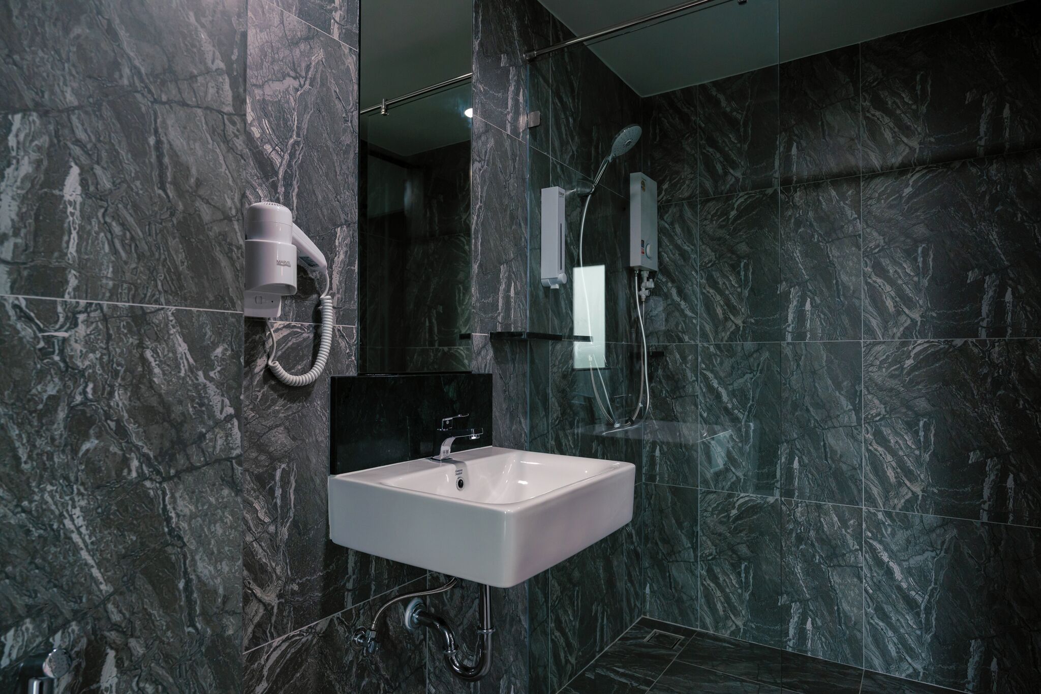 Un baño moderno con pared de mármol, lavamanos blanco, cabezal de ducha de mano y secador de pelo.