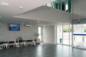 A spacious, modern waiting area with a flat-screen TV mounted on the wall, a small table with a laptop, and several white chairs. - One Budget Hotel Chiangrai Baanmai (Chiang Rai)