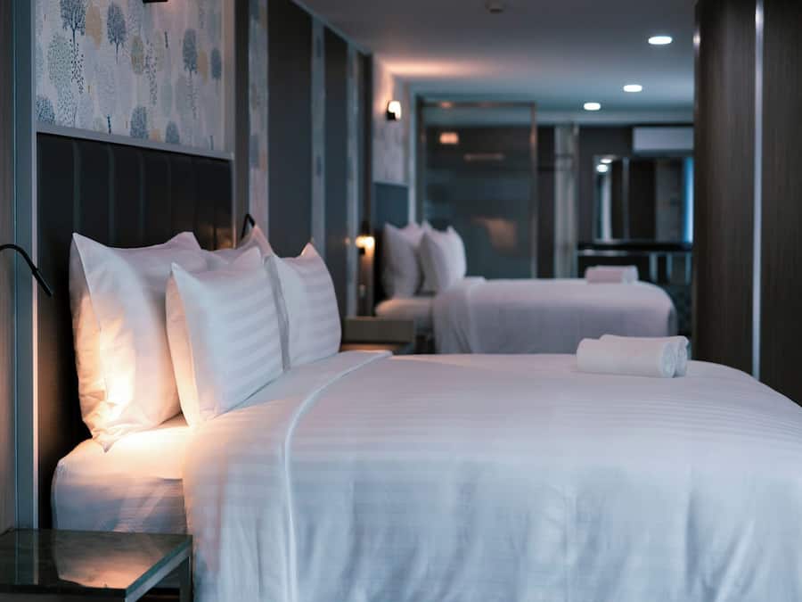 A hotel room with two beds, a bedside table, and a wall-mounted light.
