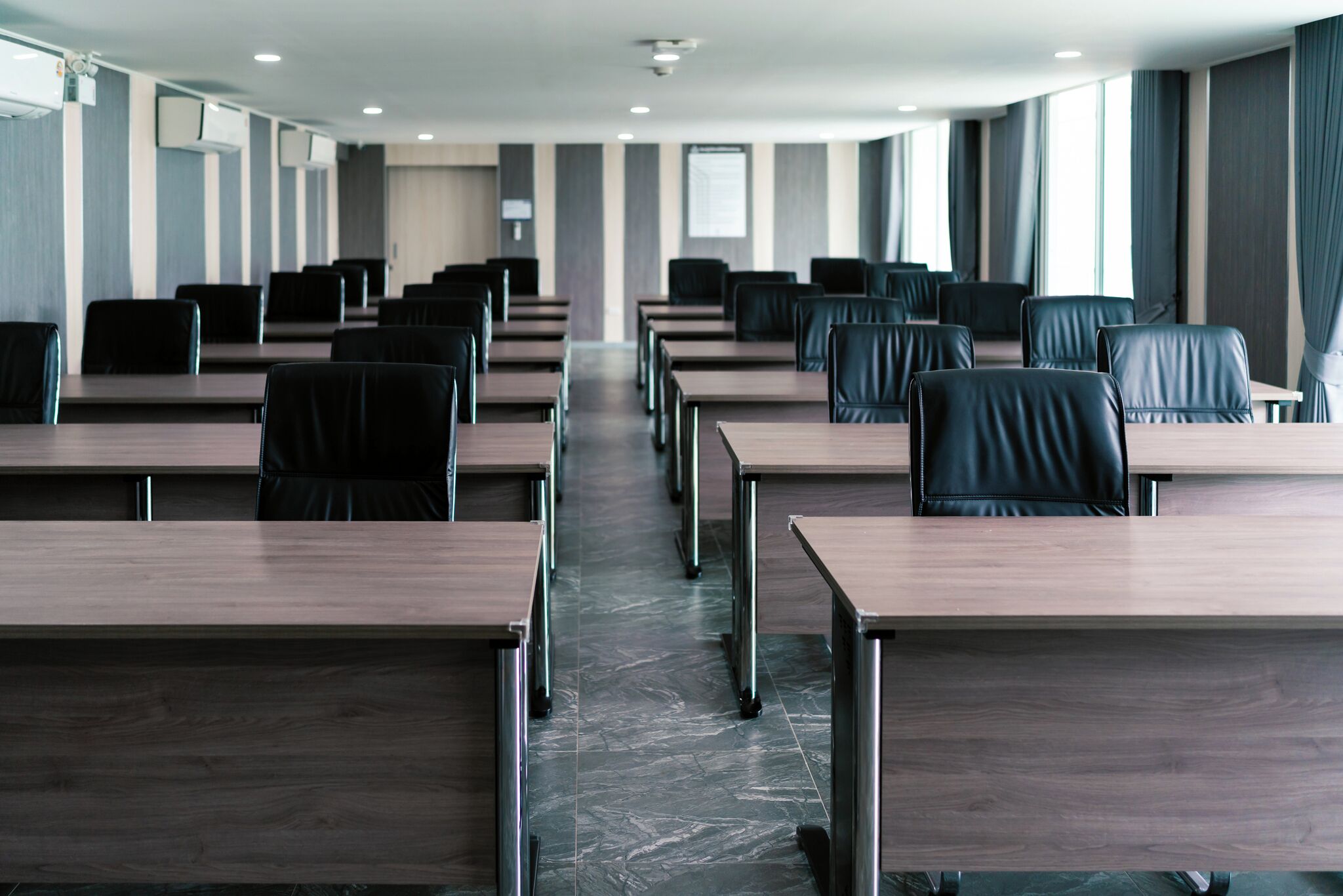 A conference room with rows of tables and chairs, large windows, and a marble floor.