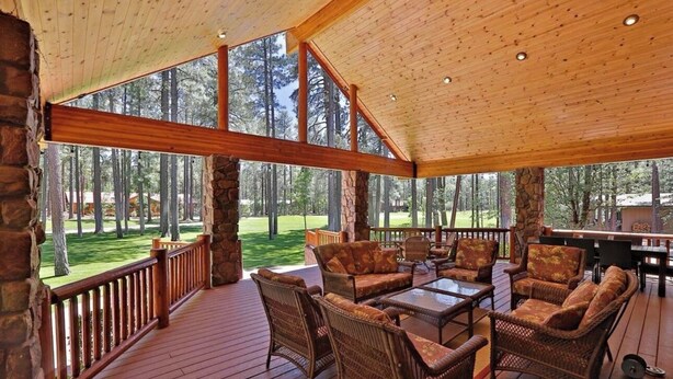 A covered outdoor deck with wicker furniture and a stone wall. - Family-friendly Pinetop cabin on Pinetop Country Club golf course (Pinetop Country Club)