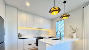 Une cuisine moderne avec des meubles blancs, un îlot central, un four encastré et des luminaires suspendus.