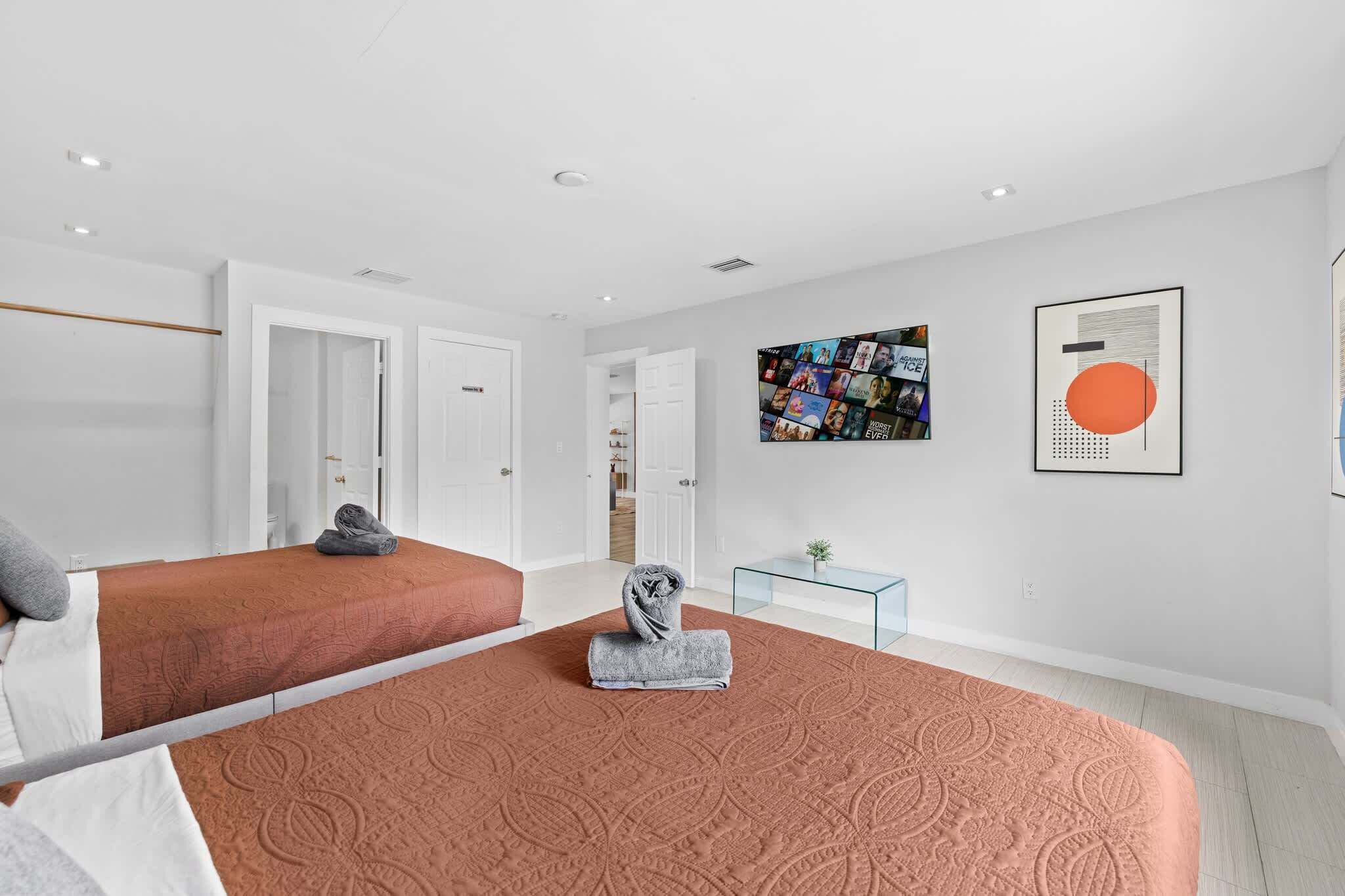 A hotel room with two beds, a glass coffee table, and artwork on the walls.
