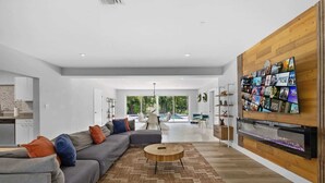 A modern living room with a sectional sofa, a coffee table, and a large TV mounted on a wooden wall. - Villa Venecia | Sand Terrace | Heated Pool | Waterfront (Miami)
