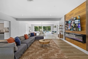 A modern living room with a sectional sofa, a coffee table, and a large TV mounted on a wooden wall. - Villa Venecia | Sand Terrace | Heated Pool | Waterfront (Miami)