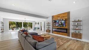 A spacious living room with a large TV, wooden panel wall, and a view of the outdoors. - Villa Venecia | Sand Terrace | Heated Pool | Waterfront (Miami)