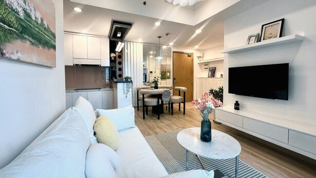 A modern living room with a white sofa, a round coffee table, and a flat-screen TV mounted on the wall.