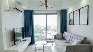 A modern living room with a flat-screen TV, a sofa, a small round table, and a view of the city through large windows.
