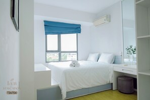 A hotel room with a bed, a desk, a window with blue curtains, and a view of buildings outside. - Masteri Thao Dien Apartment Complex (Ho Chi Minh)