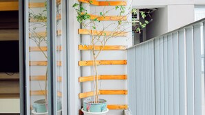 A narrow balcony with wooden flooring, potted plants, and a metal railing.
