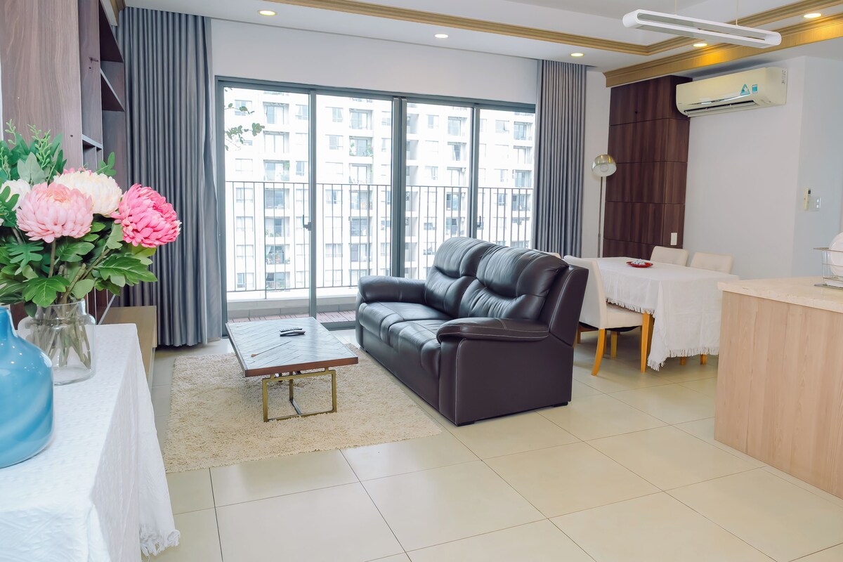 A modern living room with a leather sofa, a dining table, and a kitchen area.
