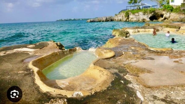 A rocky beach with clear blue water and a pool.
