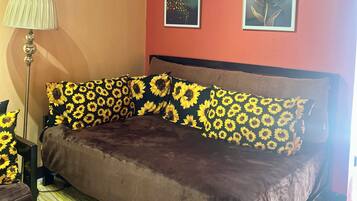 Ein Zimmer mit einem braunen Sofa, Kissen mit Sonnenblumenmuster, einer Lampe und zwei gerahmten Bildern an der Wand.