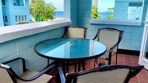 A round glass table with four chairs on a balcony with a view of the ocean.