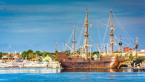 A large, historic ship docked at a marina with other boats and buildings in the background. - Beach, Don’t Kill My Vibe (Ormond Beach)