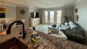 Un salon moderne comprenant un coin cuisine, une table à manger et un balcon avec vue sur la mer.
