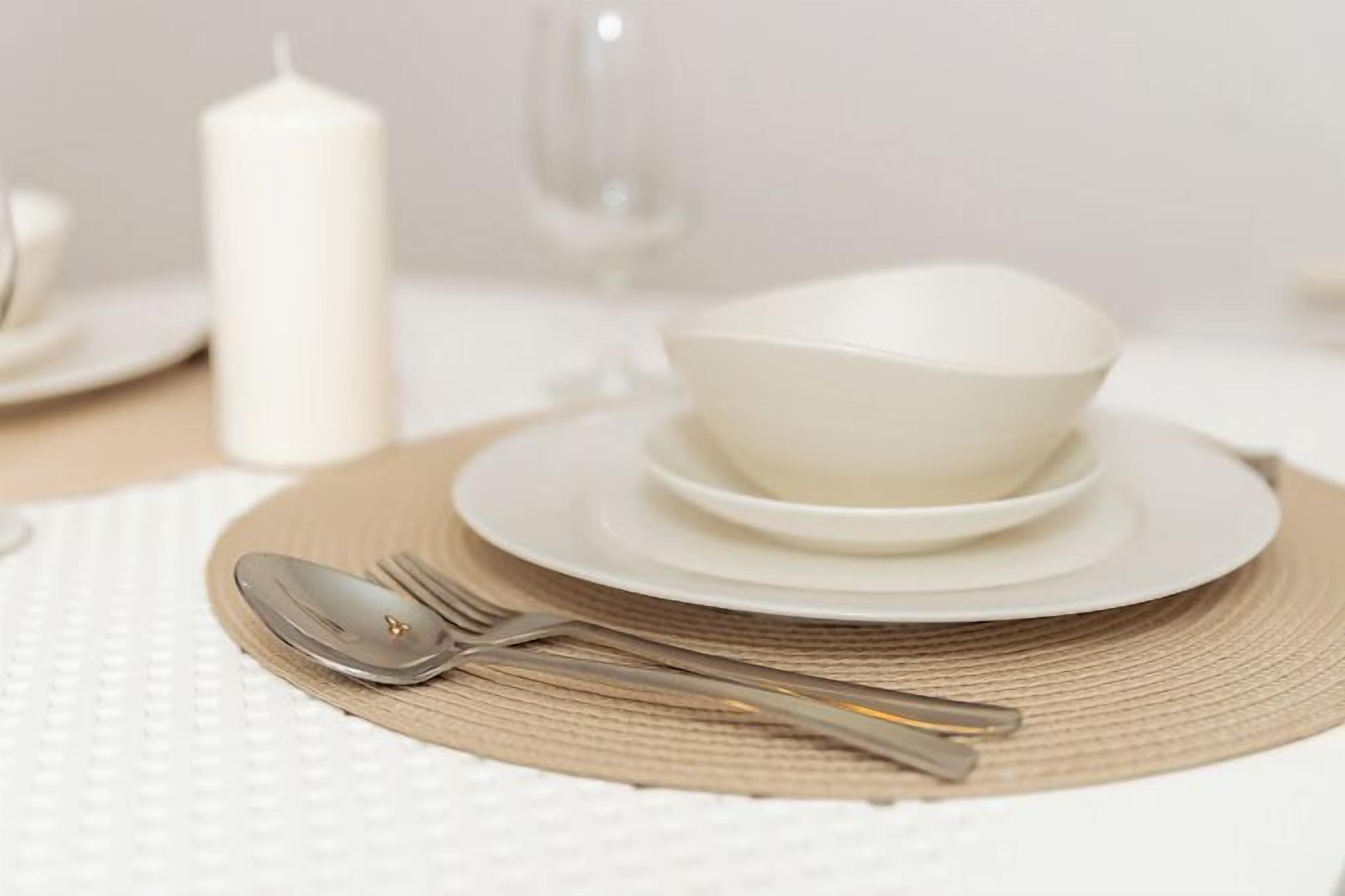 A neatly set dining table with white plates, a bowl, a spoon, and a fork on a woven placemat.