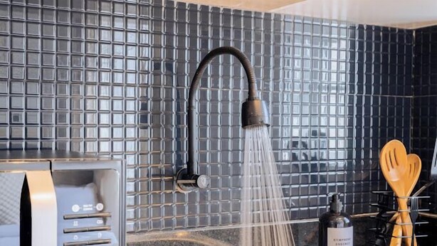 A modern kitchen with a tiled backsplash, a handheld showerhead, and a stainless steel appliance. - Lux Suites Studio City Apartments (Naivasha)