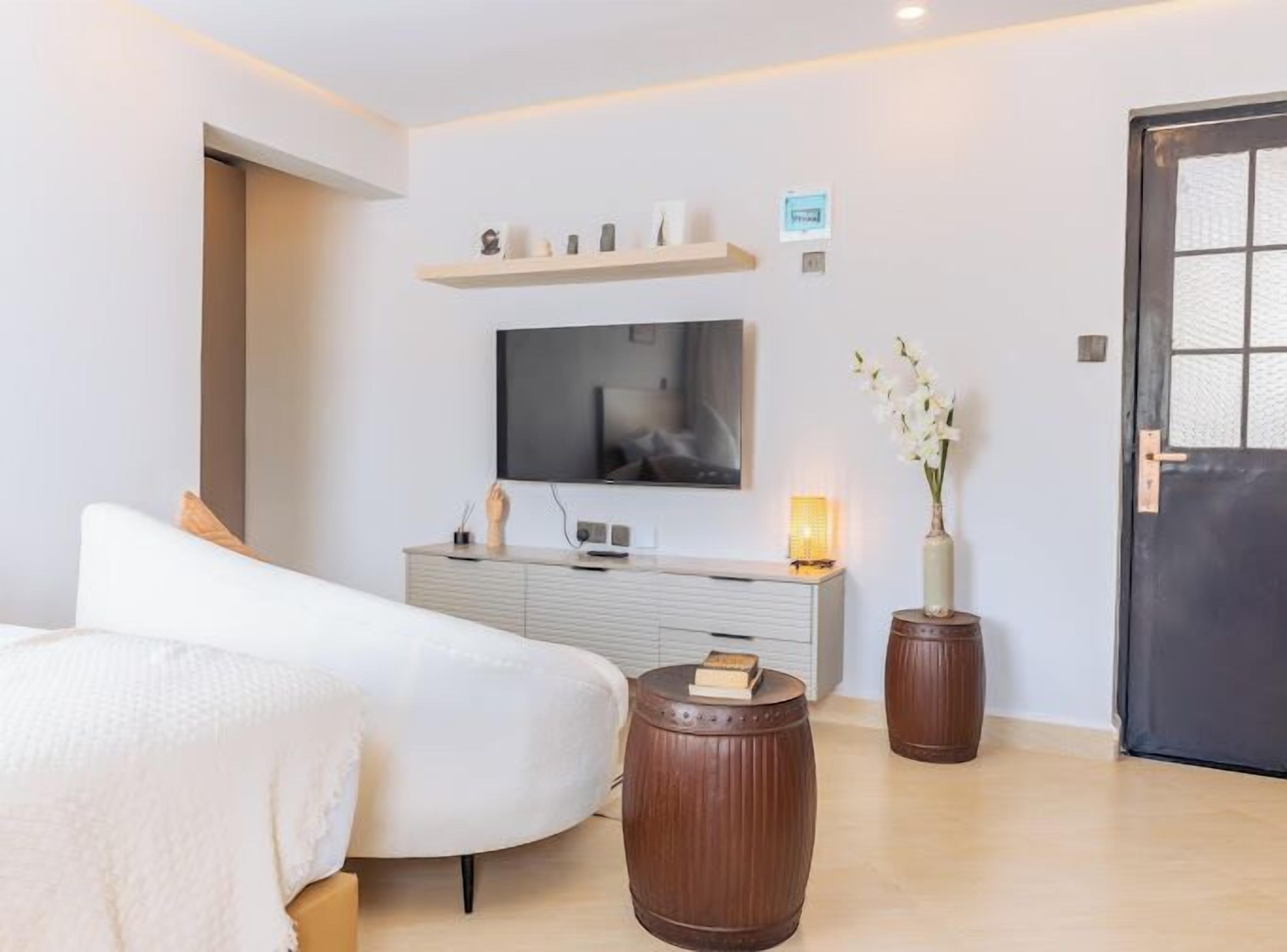 Ein modernes Schlafzimmer mit einem Bett, einem an der Wand montierten Fernseher, einem Nachttisch, einer Lampe und einer Tür.