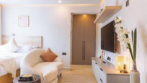 A modern bedroom with a bed, a sofa, a TV, and a bedside table. - Lux Suites Studio City Apartments (Naivasha)