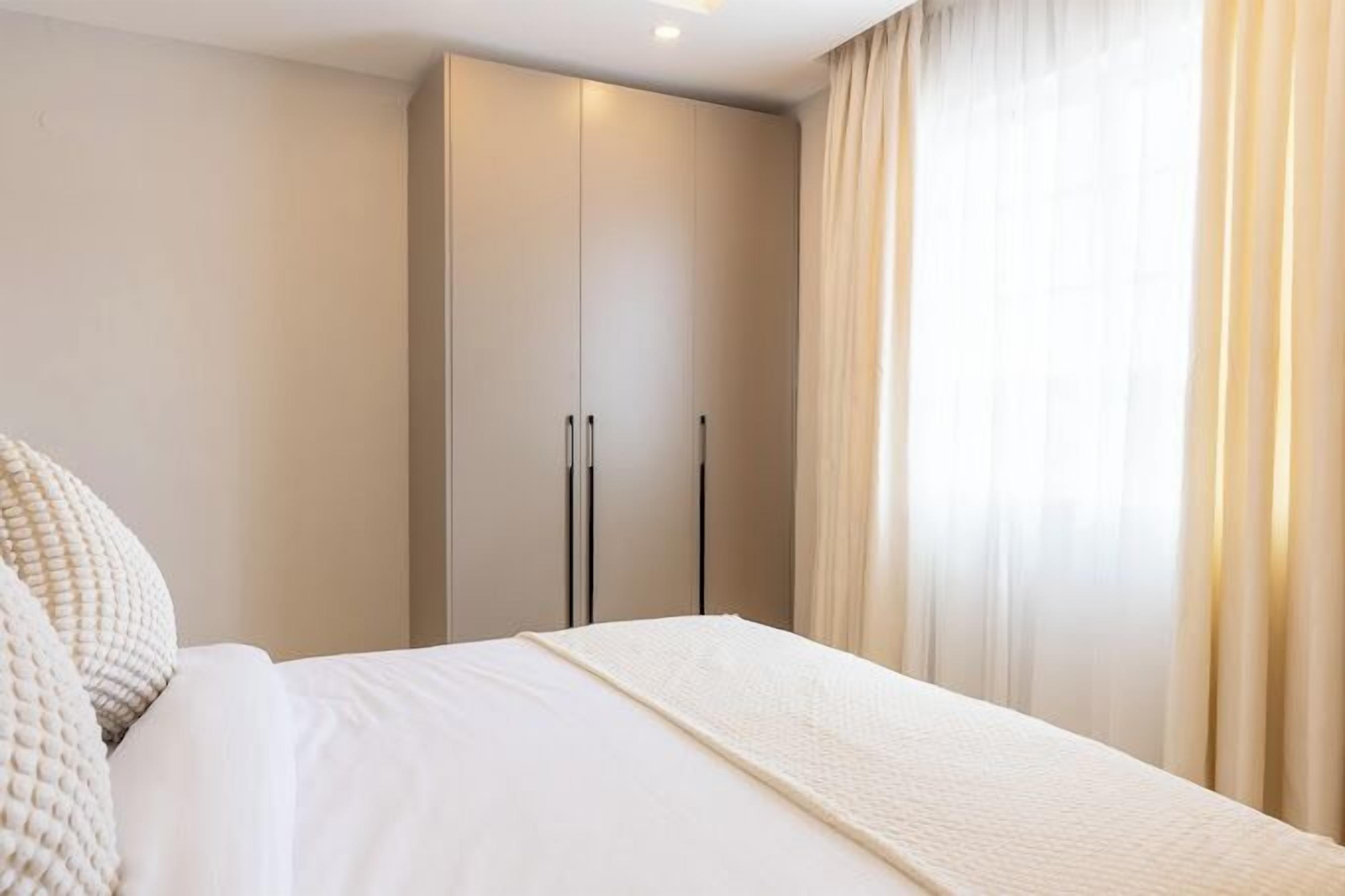 A hotel room with a large bed, a wardrobe, and sheer curtains.