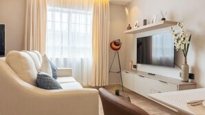 A modern living room with a sofa, a coffee table, a TV, and a decorative shelf. - Lux Suites Studio City Apartments (Naivasha)