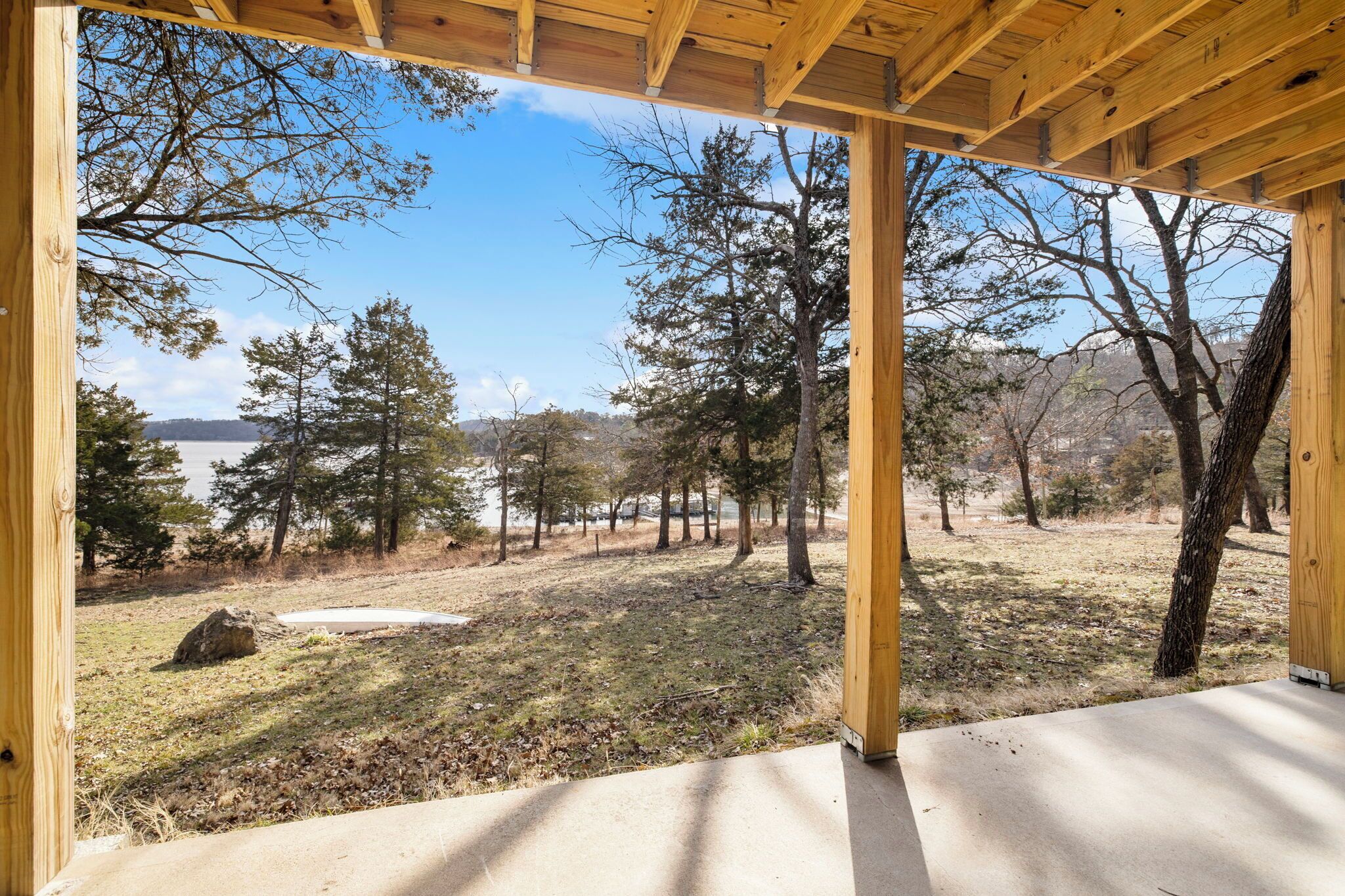 A wooden pergola structure with a view of a forested area and a body of water in the distance.