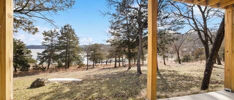 A wooden pergola structure with a view of a forested area and a body of water in the distance.