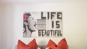 Une chambre avec un lit, des oreillers rouges, un mur orné d’une affiche du film « La vie est belle » et un mur en briques blanches.