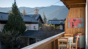 Une terrasse en bois avec deux chaises et une table, d’où l’on peut admirer un village aux maisons traditionnelles, avec une chaîne de montagnes en toile de fond.