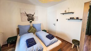 Une chambre à coucher comprenant un lit, une œuvre d’art représentant un taureau accrochée au mur, une étagère avec des articles de toilette et une armoire en bois.