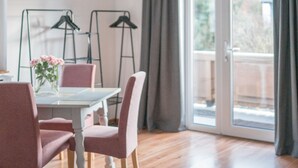 Un coin repas avec une table, des chaises et un vase de fleurs. On y trouve deux chaises noires sur des pieds et une fenêtre avec des rideaux.