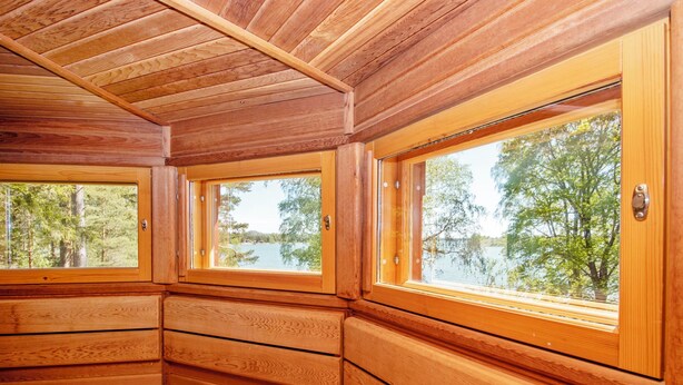 Une cabane aux murs en bois et aux grandes fenêtres, offrant une vue sur un lac et une forêt.
