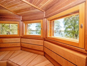 Una cabana amb parets de fusta i grans finestres que donen vista a un llac i arbres.