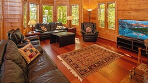 L’intérieur d’une cabane en rondins, avec un canapé en cuir, un fauteuil inclinable, une table basse et un téléviseur.