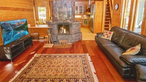 Un intérieur de chalet chaleureux avec une cheminée en pierre, un canapé en cuir, un téléviseur à écran plat et un coin repas en bois.