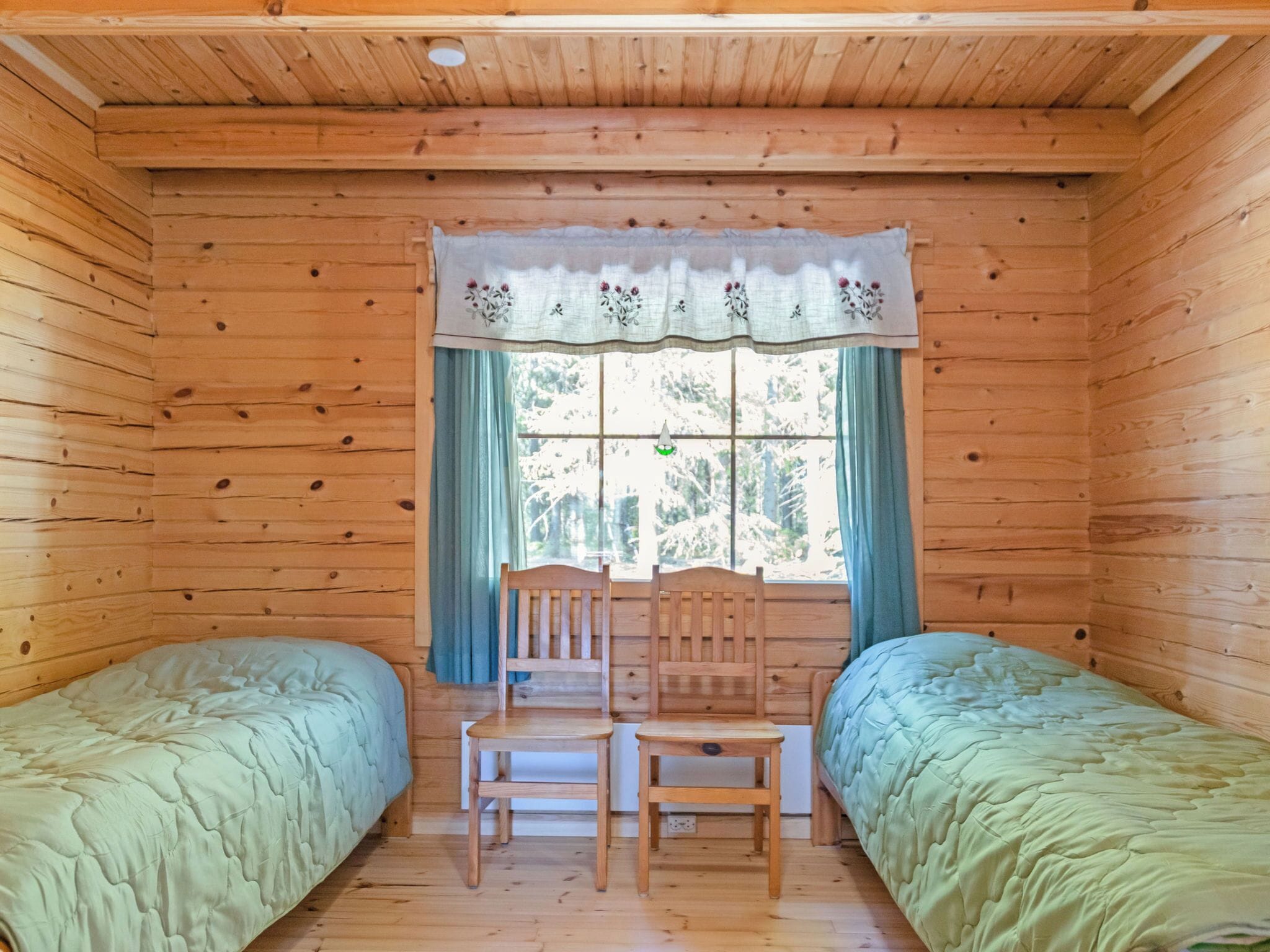 A cabin room with two single beds, a wooden chair, a table, and a window with curtains.