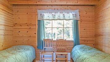 A cabin room with two single beds, a wooden chair, a table, and a window with curtains.